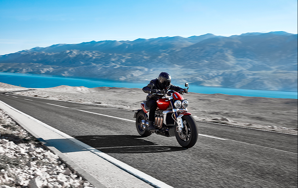 Pilotando moto na estrada com montanha e mar ao fundo